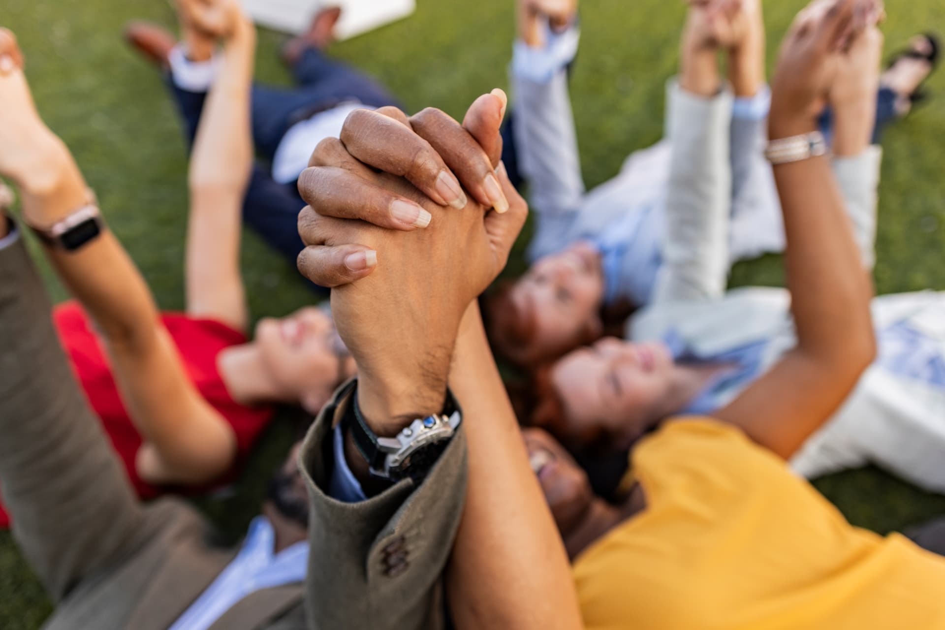 A group of people lying on grass holding hands together