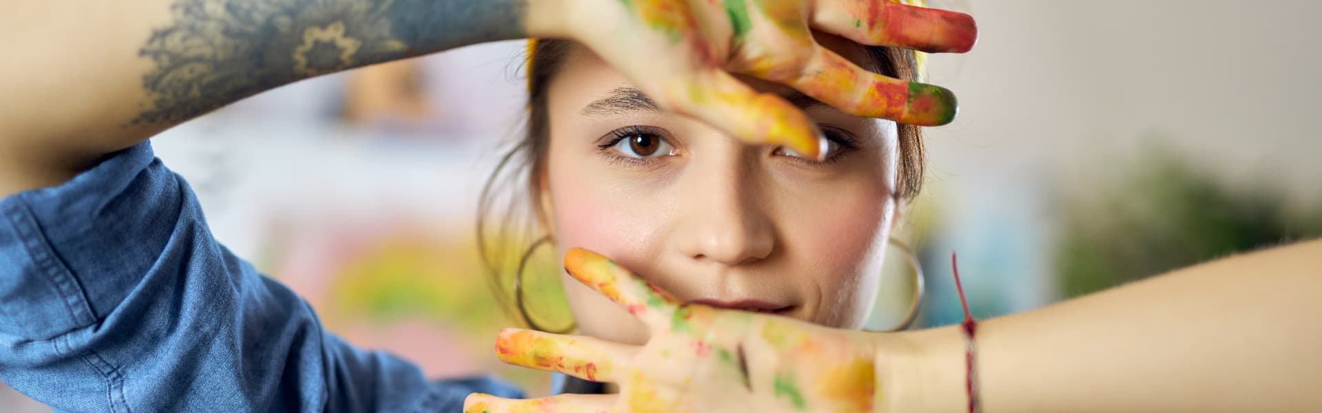 A young person with paint-covered hands framing her face